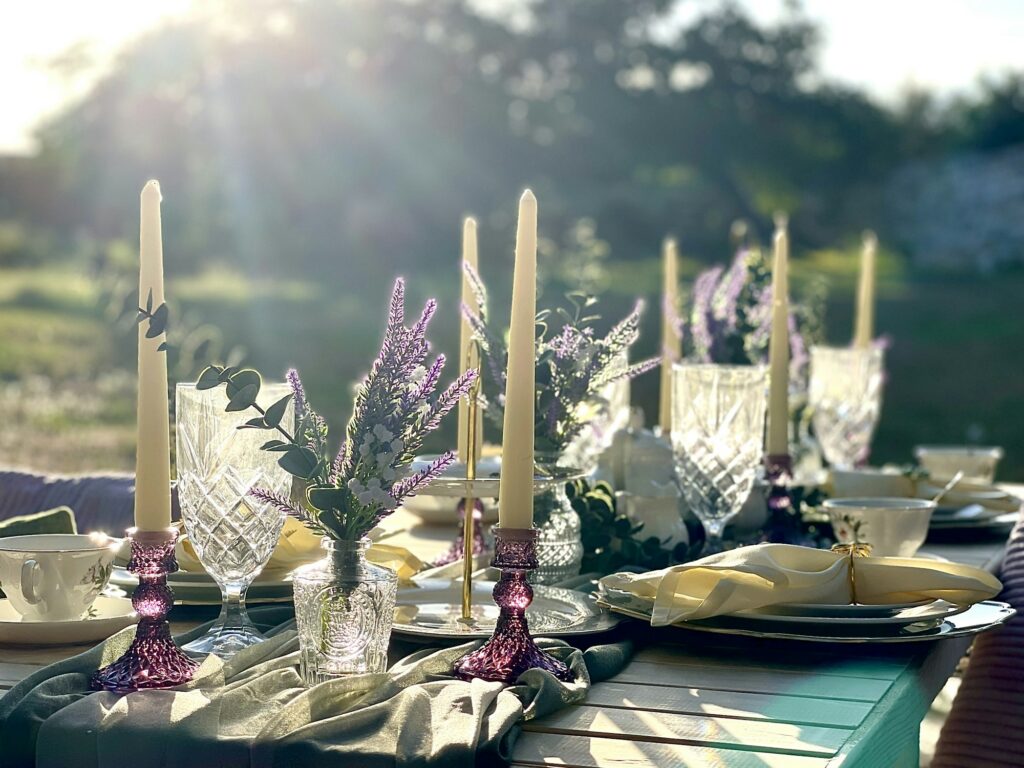 An outdoor table at golden hour, set with tall candles, wildflowers and folded napkins