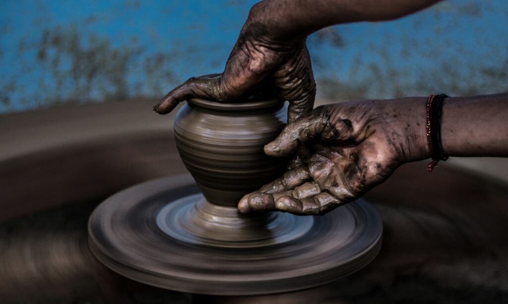Hands shaping a dark clay pot on a turning wheel